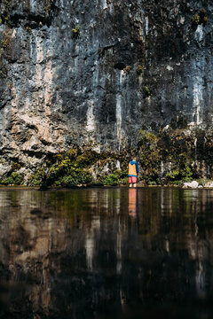 Child exploring river beneath towering cliff