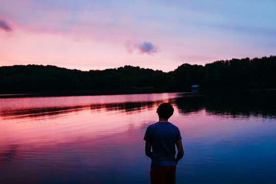 Boy watching colorful sunset over lake