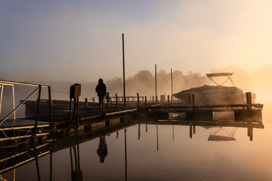 Boy fishing off foggy marina dock at sunrise
