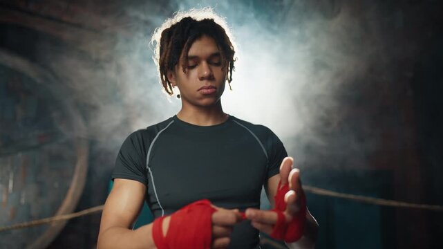 Black sportsman preparing to fight or workout in boxing club, professional sport . Portrait of african american athletic man wrapping hands by red elastic tape, protection for arms during punching