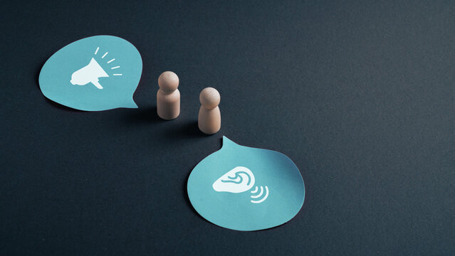 Active listening concept with wooden figures and speech bubbles showing speaking and attentive ear communication