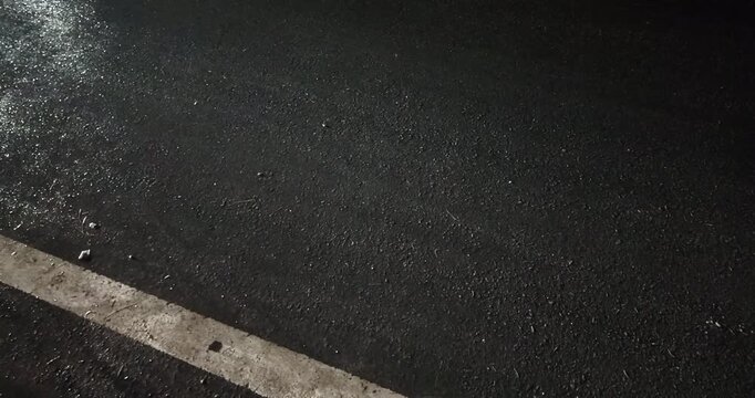 Night close up of a wet asphalt road with colorful reflections from passing cars and motorcycles right next to a white line.
