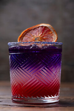 Purple layered cocktail with dried orange garnish in a textured glass
