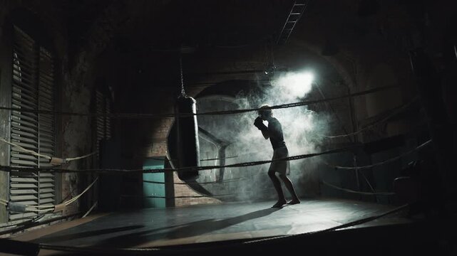Loft style interior in modern boxing club, african fighter hitting punching bag. Professional sport and physical activity for developing endurance and muscular, psychological release of aggression