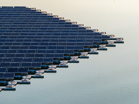 Aerial view of floating photovoltaic system with rows of solar panels on white floats over calm water during golden hour Bensheim, Hessen, Germany.