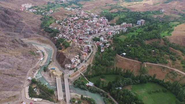 Aerial ancient hilltop fortress overlooking dense town houses in rugged valley under soft daylight. Birds eye shot stone castle tower crumbling ramparts and crowded rooftops beside river.