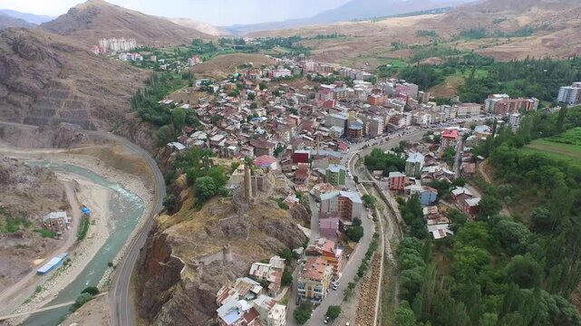 Aerial ancient hilltop fortress overlooking dense town houses in rugged valley under soft daylight. Birds eye shot stone castle tower crumbling ramparts and crowded rooftops beside river.