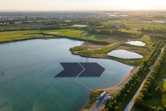 Aerial view of floating solar panels on a lake with power lines and green fields in Bensheim, Hessen, Germany.