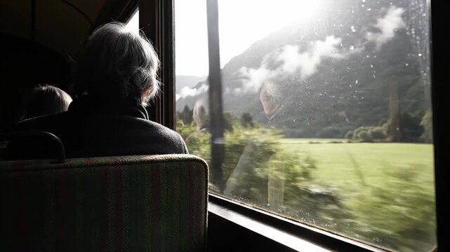 Person looking out train window at scenic landscape during daytime.