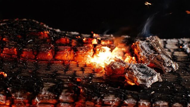 Closeup of burning wood log with glowing embers and smoke against a dark background