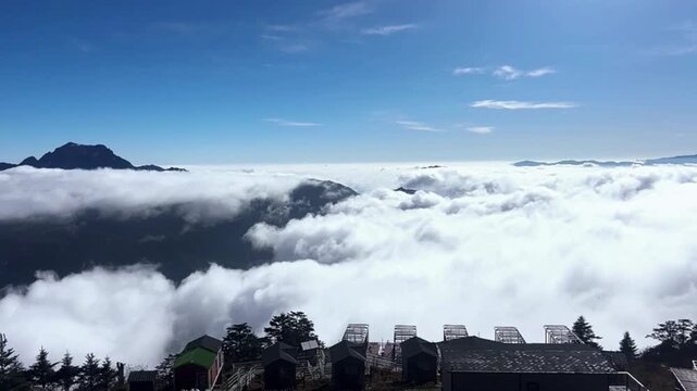 Horizontal time lapse of small cabins and viewing platforms on a mountain top surrounded by a flowing sea of clouds.