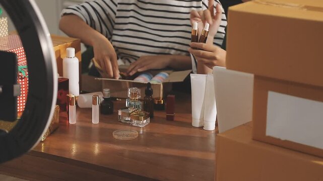 Young beautiful Asian girl reviewing cosmetic and skin care product with new collection's promotion selling on social media online live blurred phone screen surrounded beauty merchandise. Stratagem.