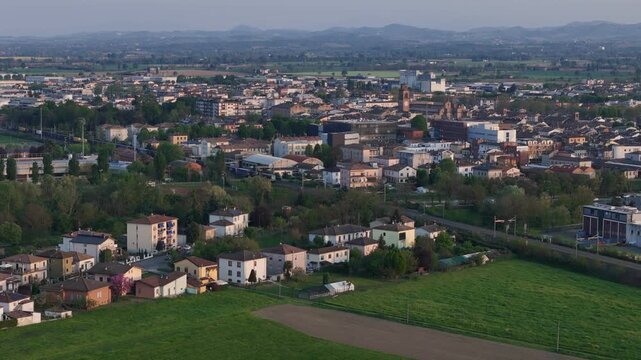 Fiorenzuola d Arda Piacenza Emilia Romagna Italy with Collegiata di San Fiorenzo, freight train on Milan Bologna railway and Po Valley farmland with Northern Apennines hills, drone pullback shot