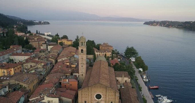 Aerial drone view of Salo town with historic church tower and terracotta roofs along Lake Garda shoreline with calm water and soft evening light in Italy