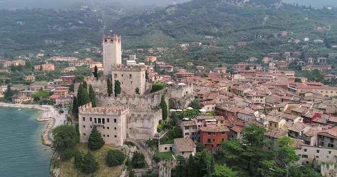 Aerial drone view of Scaligero Castle in Malcesine overlooking Lake Garda with historic stone walls tower and surrounding town with terracotta rooftops and hills