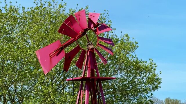 Decorative red metal windmill with green trees and blue sky in background