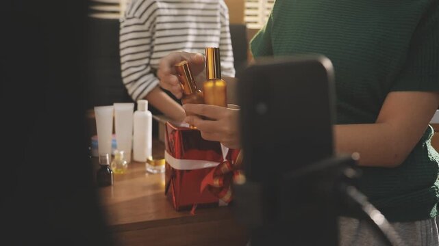 Young beautiful Asian girl reviewing cosmetic and skin care product with new collection's promotion selling on social media online live blurred phone screen surrounded beauty merchandise. Stratagem.