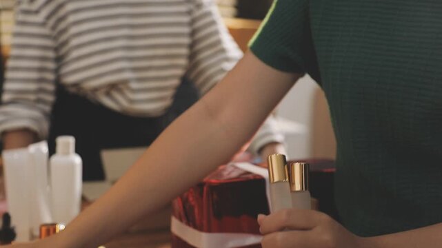 Young beautiful Asian girl reviewing cosmetic and skin care product with new collection's promotion selling on social media online live blurred phone screen surrounded beauty merchandise. Stratagem.