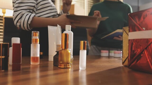 Young beautiful Asian girl reviewing cosmetic and skin care product with new collection's promotion selling on social media online live blurred phone screen surrounded beauty merchandise. Stratagem.