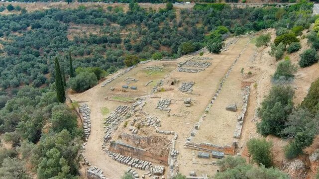Delphi, Greece. Drone footage over the ancient Sanctuary of Apollo, stone foundations and retaining walls set amid terraced olive groves on the slopes of Mount Parnassus under bright summer light. Dr