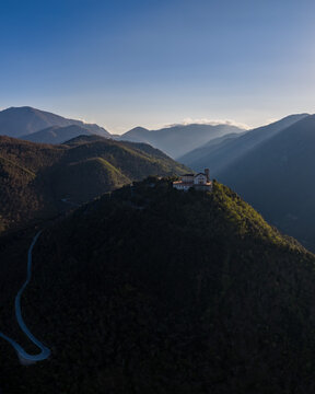 Aerial view of Santuario del Santissimo Salvatore on a mountain peak with winding roads and sunbeams over the hills in Montella, Campania, Italy.