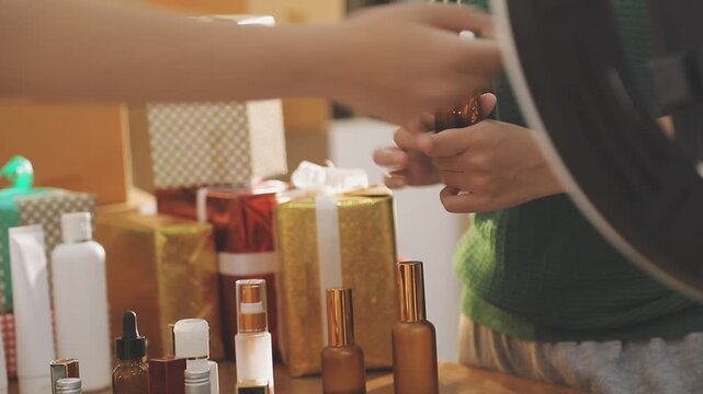 Young beautiful Asian girl reviewing cosmetic and skin care product with new collection's promotion selling on social media online live blurred phone screen surrounded beauty merchandise. Stratagem.
