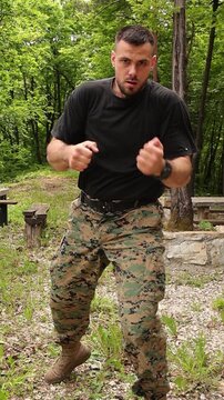 Athletic man in camouflage, tactical, military pants performs shadow boxing in a forest setting, finishing with a powerful high kick during outdoor martial arts training and self defense practice.