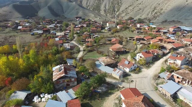 Aerial traditional village nestled in Central Anatolia region with autumn foliage and mountains. Scenic Turkish rural settlement surrounded by golden yellow trees dramatic rocky terrain fall season.