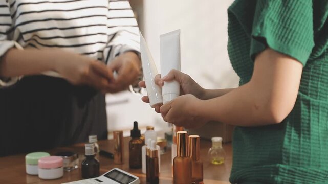Young beautiful Asian girl reviewing cosmetic and skin care product with new collection's promotion selling on social media online live blurred phone screen surrounded beauty merchandise. Stratagem.