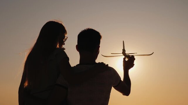 Father and daughter playing with toy plane during golden sunset at beach.