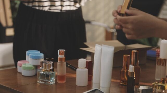 Young beautiful Asian girl reviewing cosmetic and skin care product with new collection's promotion selling on social media online live blurred phone screen surrounded beauty merchandise. Stratagem.