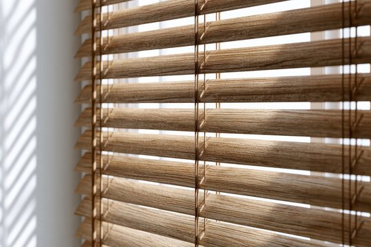 Close-up view of natural wood grain horizontal blinds filtering soft daylight, creating striped shadows.