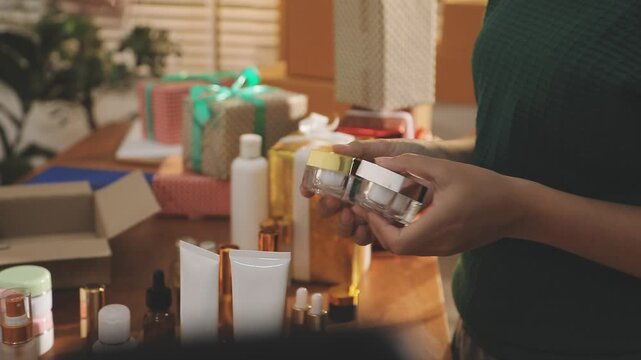 Young beautiful Asian girl reviewing cosmetic and skin care product with new collection's promotion selling on social media online live blurred phone screen surrounded beauty merchandise. Stratagem.
