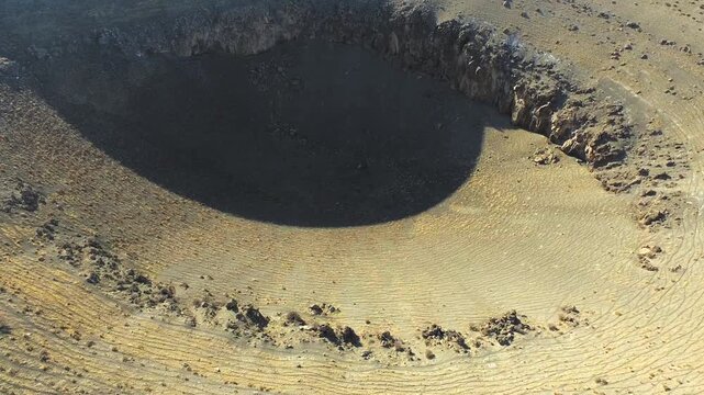 Aerial drone massive sinkhole formed by underground collapse in barren desert plain. Overhead perspective reveals circular crater, eroded edges, dry soil textures and empty arid landscape.