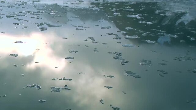 Floating ice shards dance on the placid Arctic waters. Above, a soft cloudscape mirrors the world below, casting shimmering reflections that merge with the pale blue ice.