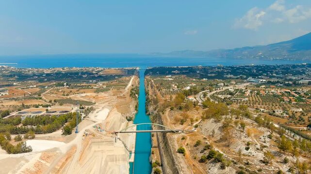 Corinth Canal, Greece. Drone footage of the narrow sea-level waterway cutting through the Isthmus, with sheer rock walls and a ship transiting under an arch bridge toward the open sea. Drone footage,