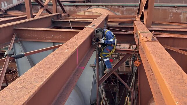 Aerial low angle shot of technician welding beams in an oil or chemical refinery. Industrial rope access worker descends to sand and repair structure. Working at height. Rappelling.