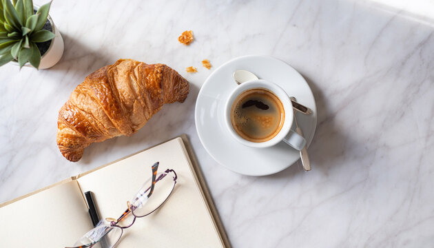 Overhead flat lay of morning coffee and breakfast on marble table with notebook