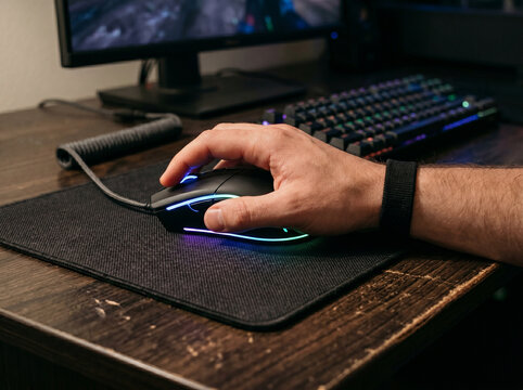 Hand Using An Illuminated Wired Gaming Mouse On A Dark Wooden Desk