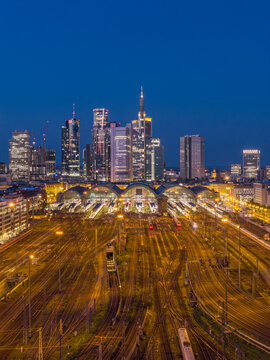 Aerial view of Hauptbahnhof central station with illuminated train tracks and the modern city skyline under a blue hour sky Frankfurt am Main, Hessen, Germany.