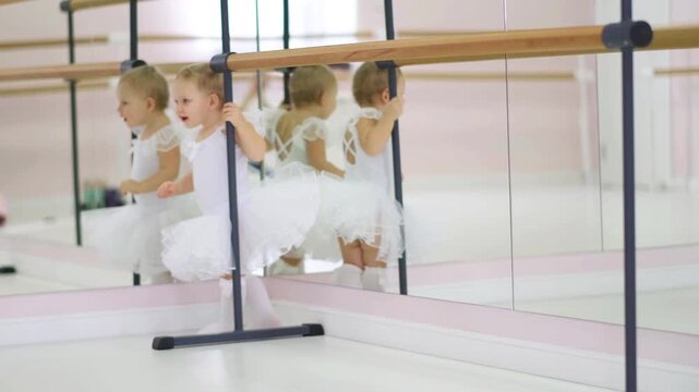 Little girl in a white tutu holding onto a ballet barre, learning to dance. Early childhood development and dance school lesson.