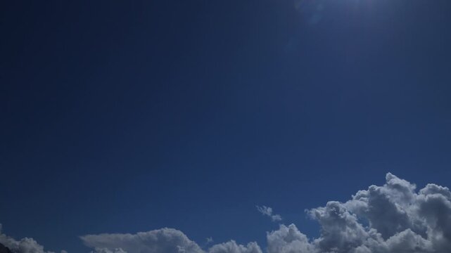 Blue bright sky with cumulus clouds moving and changing shape on the lower edge of the frame. Time-Lapse sky only video with copy space