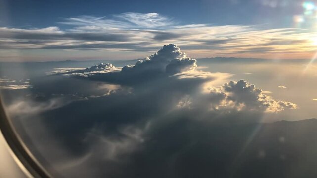 Epic view from a plane window showing bright sun illuminating layered clouds, mountains and blue sky