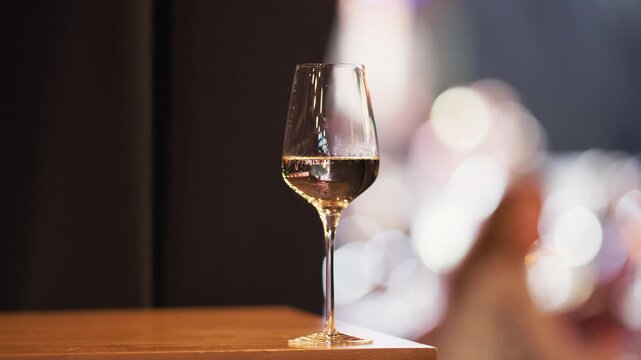 Quiet relaxing space showcasing single wine glass amidst gentle lighting and blurred crowd in background