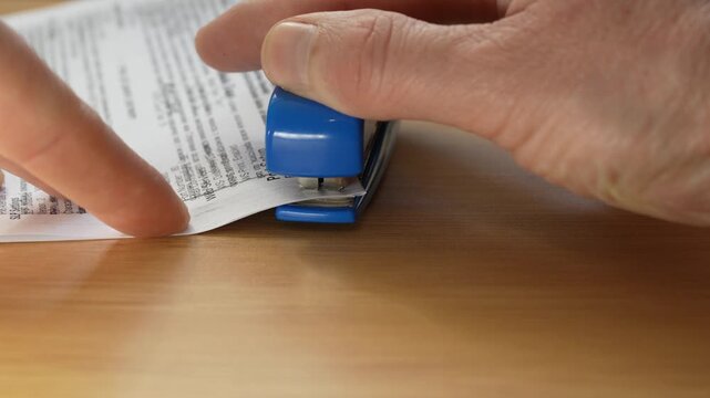 Close up of male hands stapling paper documents on desk. Concept of office workflow, paperwork, documentation and administrative tasks.