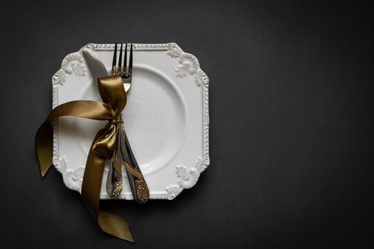 Romantic tabble setting with ribbon, plates, cutlery on black background. Empty plate. Mockup design layout for your text. Love romantic concept. Copy space. Top view. Flat lay.