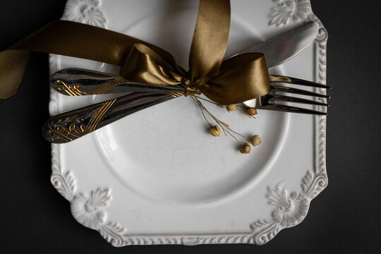 Romantic tabble setting with ribbon, plates, cutlery on black background. Empty plate. Mockup design layout for your text. Love romantic concept. Copy space. Top view. Flat lay.
