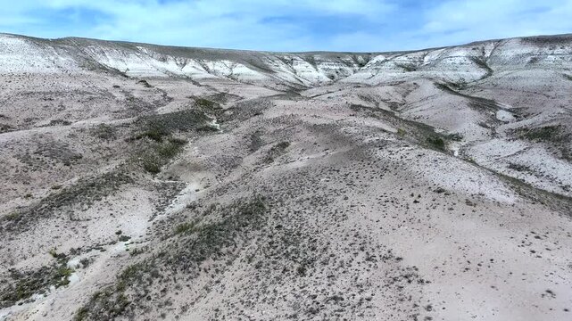 Pale badlands spread across a desert valley, revealing eroded gullies and limestone hills. Barren channels and dusty landforms create a stark geological scene with survey friendly texture.