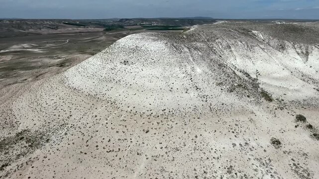 Ancient burial mound rises from a treeless hill, showing oval form in a dry open landscape. Earthen tumulus and stony steppe create an archaeological scene with isolated terrain and history.
