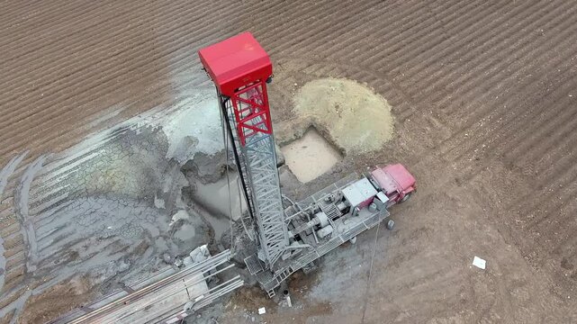 Workers drill a water well in farmland, surrounding the rig with trucks and field equipment. Borehole crew and rural machinery create an industrial agriculture scene with practical purpose.